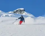 Skifahrer in roter Hose und blauer Jacke wirbelt Schnee auf. Die Columbia Omni-Heat Erfahrung: warm und trocken im Pulverschnee.