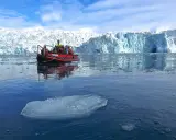 Ein Schlauchboot mit Touristen fährt auf dem eisigen Meer vor einem riesigen Gletscher. Ein wahrer "ice express" in die Arktis.