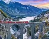 Roter Zug überquert eine Steinbrücke in verschneiter Schweizer Alpenlandschaft. Ein perfektes reiseziel schweiz.