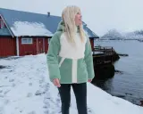 Frau in flauschiger Fleecejacke, bereit für das **fleece waschen**, steht vor rotem Haus am Meer.