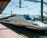 Moderner, weißer Renfe ave zug mit lila Akzenten steht auf Gleisen unter einem Bahnhofsdach.