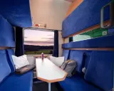 Gemütliche Kabine im Holland Zug mit blauen Sitzen, einem Tisch und Blick auf die Landschaft bei Sonnenuntergang.