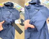 Blaue Regenjacke reparieren: Ein Loch im Ärmel wird mit einem Reparaturflicken ausgebessert. Zubehör für die Regenjacke liegt bereit.