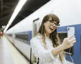 Junge Frau mit Kopfhörern macht ein Selfie am Bahnhof. Sie freut sich, ihr nächstes Abenteuer mit dem **discover eu pass** zu beginnen.