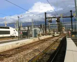 Ein weißer Hochgeschwindigkeitszug steht am Bahnsteig. Die Gleise führen in die Ferne, vorbei an Signalen und Oberleitungen. Vielleicht ist dies der **Zug nach Barcelona**?