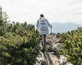 Frau wandert mit Baby im Tragetuch auf einem felsigen Bergpfad, umgeben von grünen Kiefern.