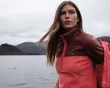 Frau mit langen Haaren im Zwiebel-Look, trägt eine zweifarbige Fleecejacke von Columbia am Seeufer.