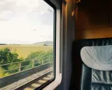 Blick aus dem Zugfenster auf grüne Felder und Hügel. Bequemer Sitzplatz im Abteil, bereit für die Reise durch den Euro city.