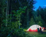 Ein beleuchtetes Zelt in einem dunklen Wald, ein Mann bereitet sich auf die Nacht vor. Perfekt für Trekking Camps Deutschland.