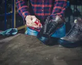 Mann pflegt Hanwag Schuhe mit einem roten Pflegeprodukt. Ein blaues Tuch liegt daneben.