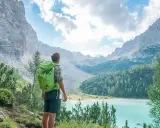 Wanderer mit Rucksack blickt auf türkisfarbenen Bergsee. Die Alpenlandschaft erinnert an die Grenze zwischen Schweiz und Italien.