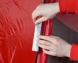 Hände reparieren ein rotes Zelt mit Klebeband.