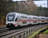 Ein moderner Doppelstockzug der Deutschen Bahn fährt durch eine herbstliche Landschaft. Die roten Streifen am Zug heben sich vom silbernen Lack ab.