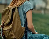 Mädchen mit braunem Rucksack sitzt im Gras. Der Rucksack ist bereit für das Waschen, um ihn wieder frisch zu machen.
