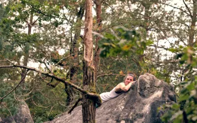 Frau ruht sich nach dem Fontainebleau Bouldern auf einem Felsen aus, umgeben von Bäumen.