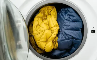 Zwei Daunenjacken, eine gelbe und eine blaue, warten darauf, in der Waschmaschine gewaschen zu werden.