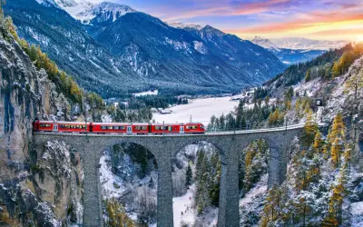 Roter Zug überquert eine Steinbrücke in verschneiter Schweizer Alpenlandschaft. Ein perfektes reiseziel schweiz.