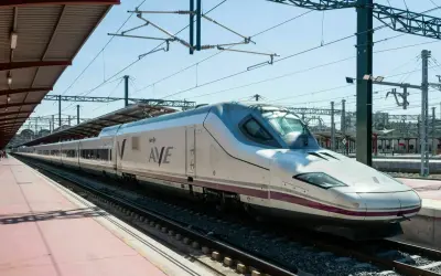 Moderner, weißer Renfe ave zug mit lila Akzenten steht auf Gleisen unter einem Bahnhofsdach.