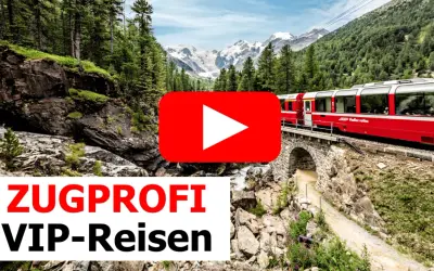 Ein roter Panoramazug fährt über eine Steinbrücke durch eine Berglandschaft mit Wäldern und schneebedeckten Gipfeln.