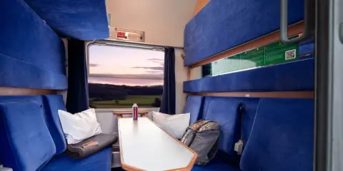 Gemütliche Kabine im Holland Zug mit blauen Sitzen, einem Tisch und Blick auf die Landschaft bei Sonnenuntergang.