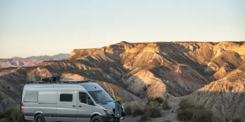 Ein Campervan steht in der Wüste Spaniens, bereit für wildcampen. Die Sonne beleuchtet die zerklüfteten Berge im Hintergrund.