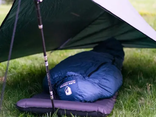 Ein dunkelblauer Kunstfaser-Schlafsack liegt auf einer Isomatte unter einem Tarp. Perfekt für Outdoor-Abenteuer, auch wenn man ihn mal waschen muss.
