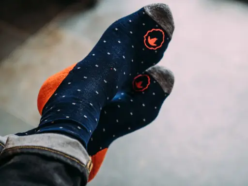Blaue Socken mit orangen Akzenten und kleinen weißen Punkten. Die Socken haben ein rotes Logo und sind aus Merinowolle, ideal zum Waschen.
