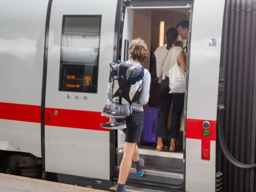 Reisende steigen in den ICE ein, um die ICE strecken zu befahren. Ein junger Mann mit Rucksack und Schuhen am Gepäck steigt als Erster ein.