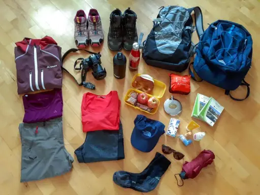Packliste Mehrtagswanderung: Wanderschuhe, Rucksäcke, Kleidung, Kamera, Verpflegung, Trinkflasche, Sonnenbrille, Regenschirm und Wanderkarten.