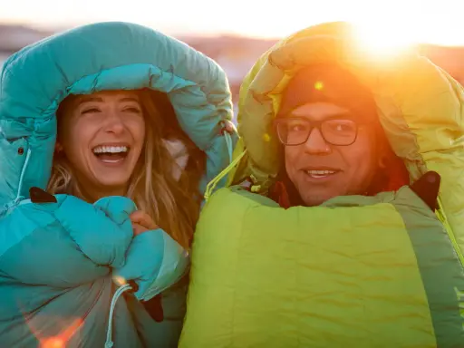 Glückliches Paar in Schlafsäcken bei Sonnenuntergang. Die Frage welcher Schlafsack bei welcher Temperatur ist hier wohl gelöst!