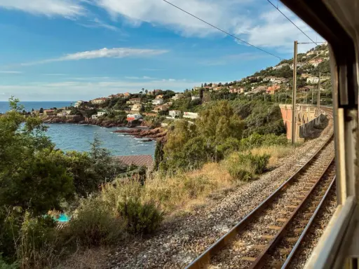 Blick aus dem Fenster eines Nachtzugs Paris Nizza auf eine Küstenlandschaft mit Häusern, Meer und Bahngleisen.