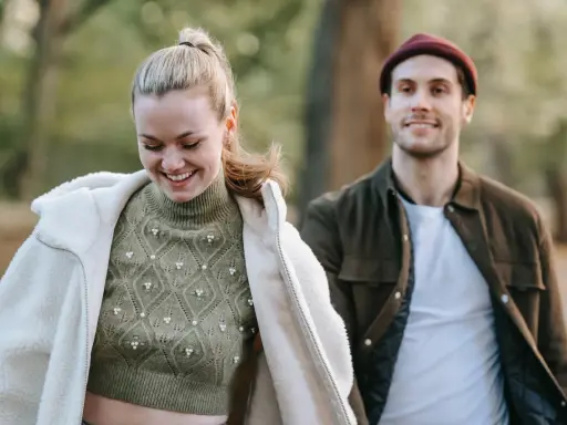 Ein lächelndes Paar im Freien. Sie trägt einen Strickpullover und eine Lammfelljacke, er eine Jacke und Mütze. Perfekt, um was anziehen bei 15 Grad.