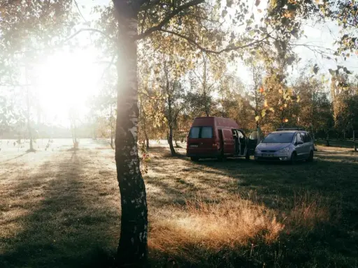 Sonnenaufgang im Herbst. Ein roter Camper und ein silberner Van stehen auf einer Wiese. Das ist Freiheit, das ist was ist wildcampen.