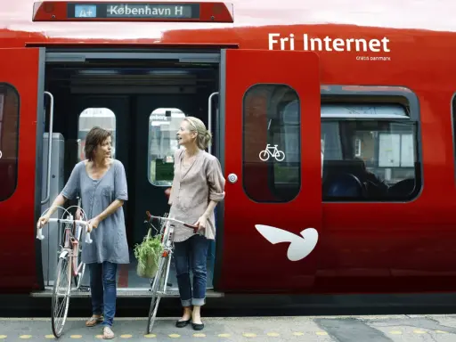 Zwei Frauen mit Fahrrädern steigen in einen roten **denmark train** nach Kopenhagen.