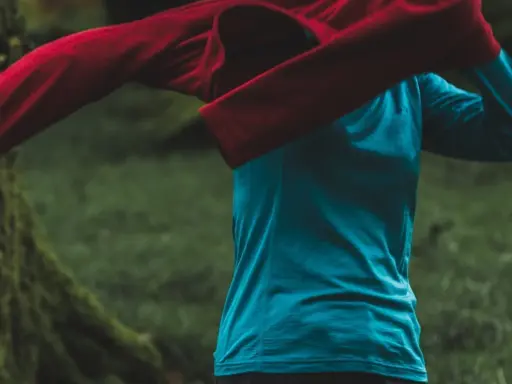 Person zieht ein rotes Oberteil über ein blaues Funktionsshirt. Das blaue Shirt ist ein Baselayer, der die Körperwärme reguliert.