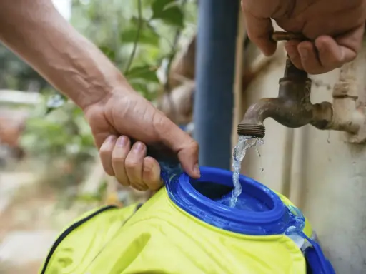 Wasser fließt aus einem alten Wasserhahn in eine gelbe Trinkblase. Nach dem Befüllen muss die Trinkblase trocknen.