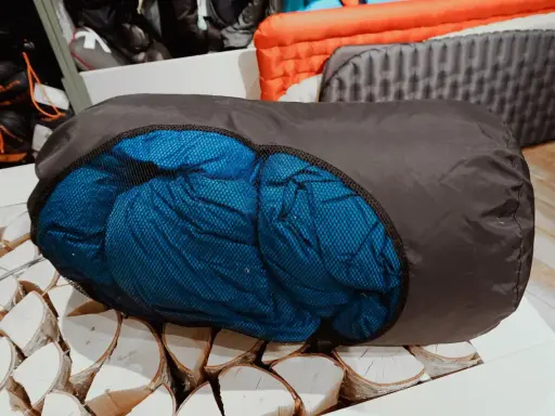 Ein blauer Schlafsack wird in einen dunklen Packsack gestopft, bereit für das nächste Abenteuer.