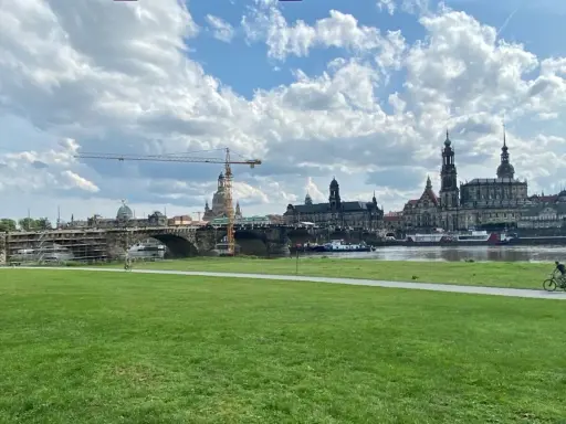 Grüne Wiese mit Blick auf die Elbe, die Brücke und die Frauenkirche. Ein Radfahrer genießt die Aussicht, um Dresden zu erleben.