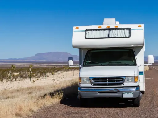 Weißer Freeway Camper steht am Straßenrand in karger Landschaft mit Bergen am Horizont.