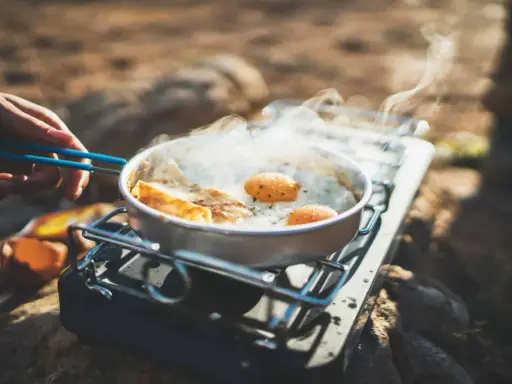 Spiegeleier und Brot brutzeln in einer Pfanne auf einem Gaskocher. Perfekte Camping Rezepte für unterwegs.
