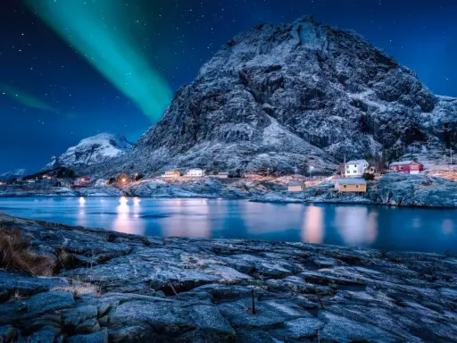 Ein malerisches Dorf in Norwegen im Winter, beleuchtet von den Nordlichtern und dem Sternenhimmel.