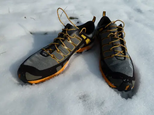 Graue und orangefarbene trailrunningschuhe zum wandern liegen im Schnee.