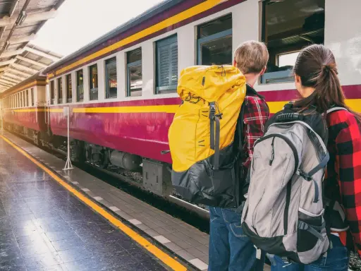 Zwei Rucksacktouristen warten am Bahnsteig auf ihren Zug. Mit ihrem world pass sind sie bereit für neue Abenteuer.