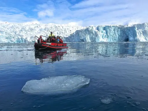 Ein Schlauchboot mit Touristen fährt auf dem eisigen Meer vor einem riesigen Gletscher. Ein wahrer "ice express" in die Arktis.