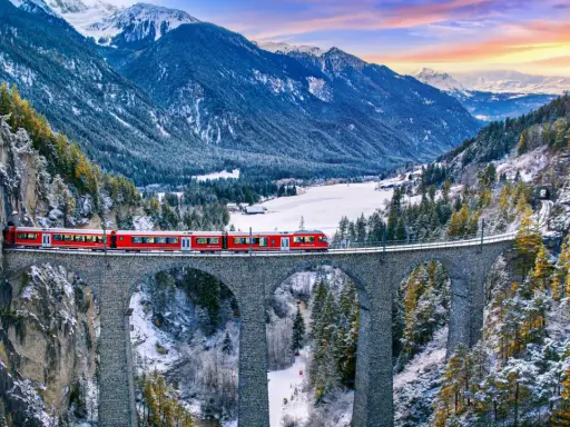Roter Zug überquert eine Steinbrücke in verschneiter Schweizer Alpenlandschaft. Ein perfektes reiseziel schweiz.