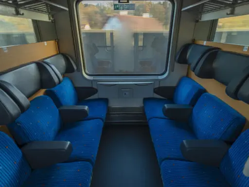 Leere Sitze im Nachtzug nach Stockholm. Blaue Polster mit orangefarbenen Punkten und schwarze Armlehnen laden zur Reise ein.