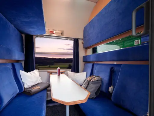 Gemütliche Kabine im Holland Zug mit blauen Sitzen, einem Tisch und Blick auf die Landschaft bei Sonnenuntergang.