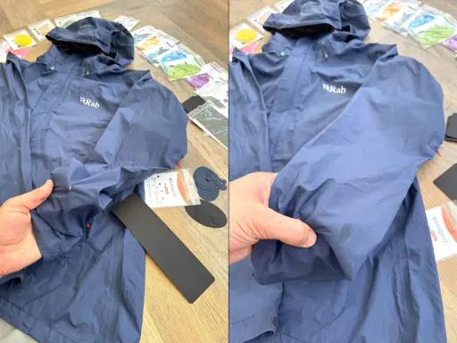 Blaue Regenjacke reparieren: Ein Loch im Ärmel wird mit einem Reparaturflicken ausgebessert. Zubehör für die Regenjacke liegt bereit.