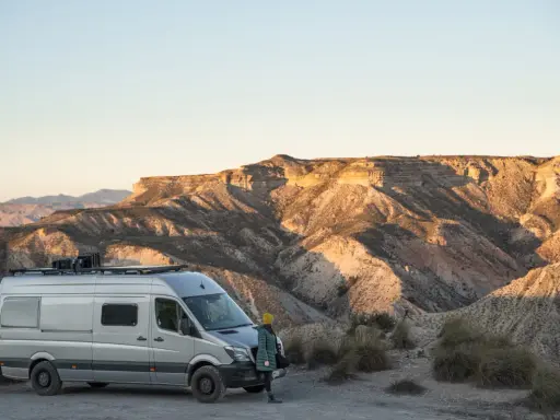 Ein Campervan steht in der Wüste Spaniens, bereit für wildcampen. Die Sonne beleuchtet die zerklüfteten Berge im Hintergrund.