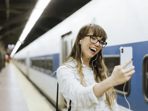 Junge Frau mit Kopfhörern macht ein Selfie am Bahnhof. Sie freut sich, ihr nächstes Abenteuer mit dem **discover eu pass** zu beginnen.
